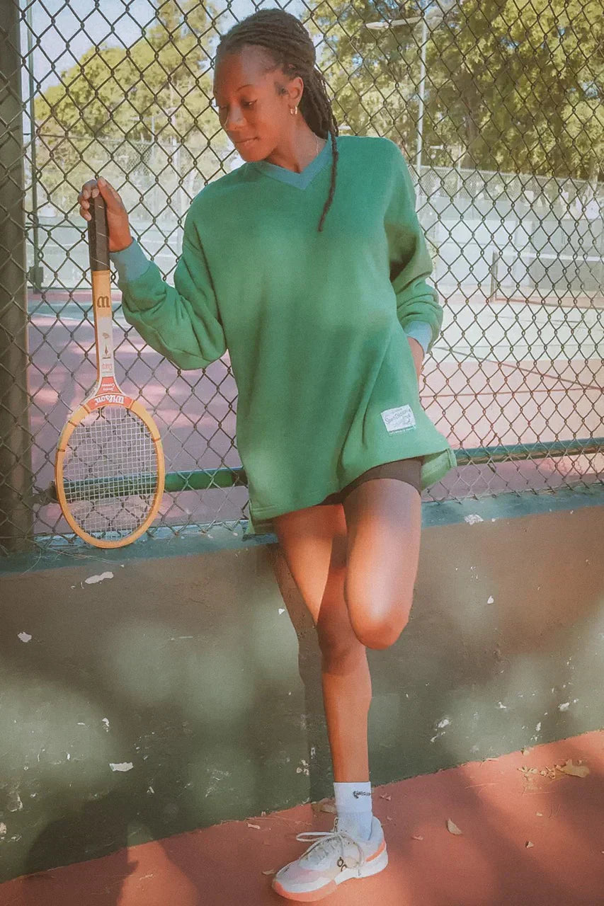 female tennis player stretching on a tennis court wearing ace the moon pullover sweatshirt