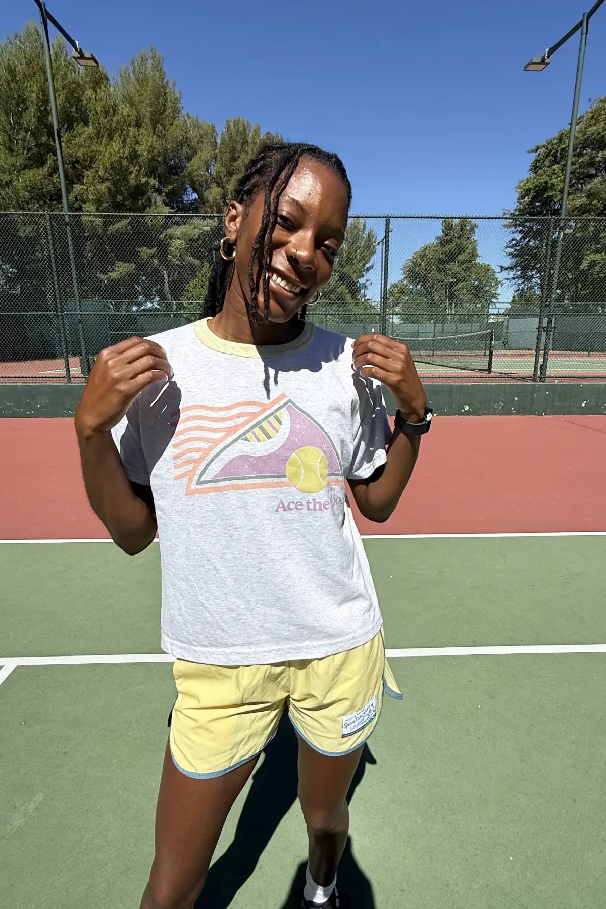 female tennis player holding a tennis ball out to the camera wearing ace the moon tennis shorts