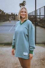 Woman wearing a teal sweater standing on a tennis court.