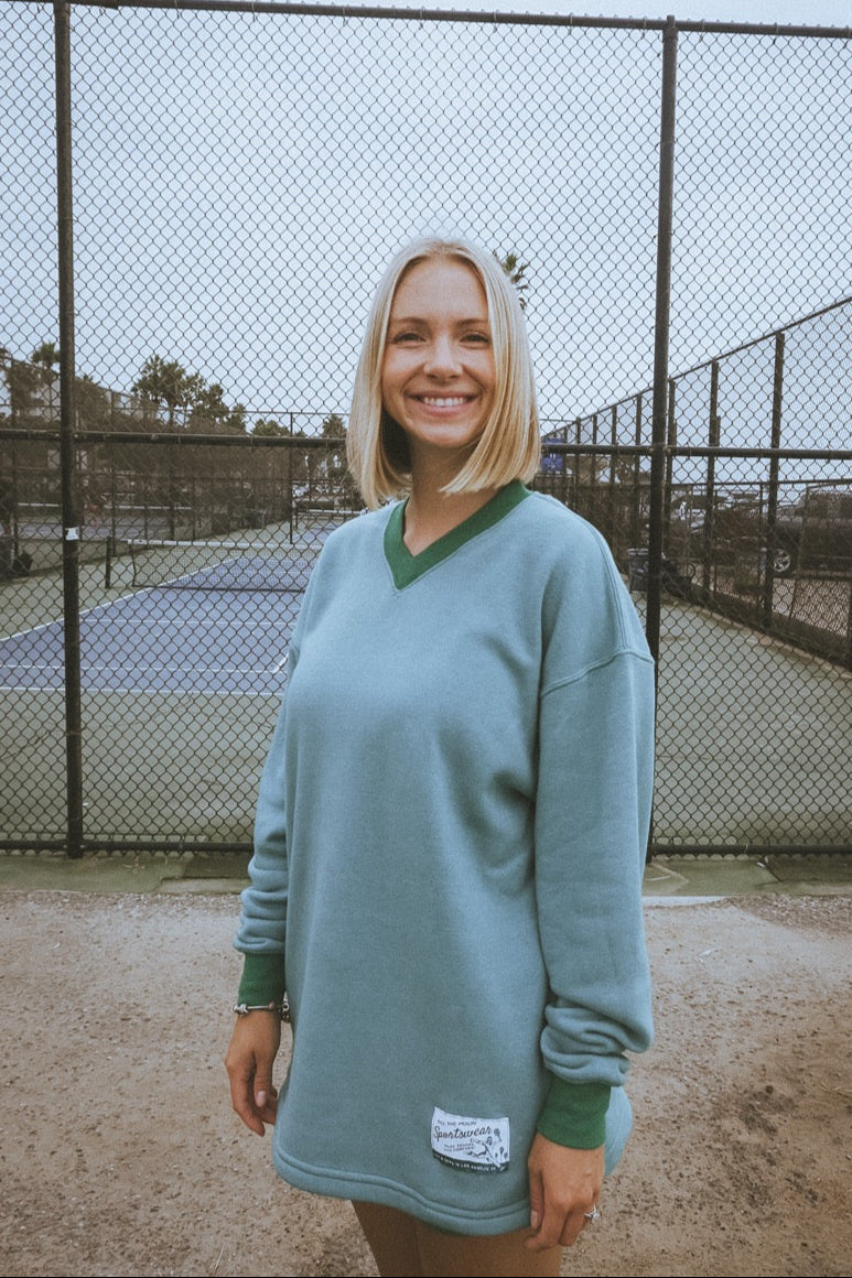 Woman wearing a green sweater standing in front of a chain-link fence.
