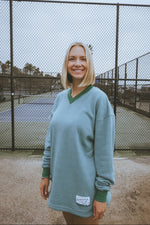 Woman wearing a green sweater standing in front of a chain-link fence.