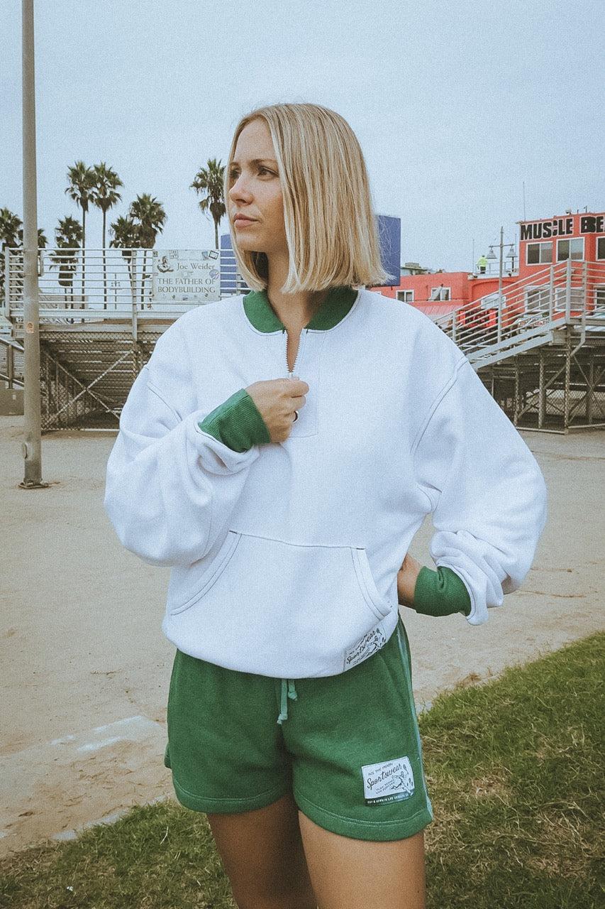 Woman wearing a white and green outfit with palm trees and a building in the background