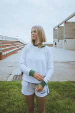 Person wearing a white sweatshirt with green accents outdoors on a grassy area.