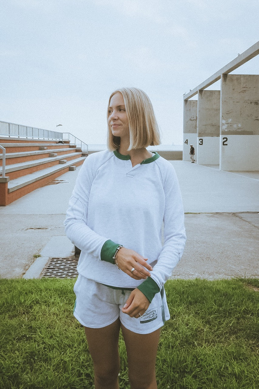 Person wearing a white sweatshirt with green accents outdoors on a grassy area.