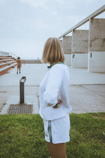 Person standing with a view of a building and another person in the distance by the ocean in california wearing ace the moon tennis henley
