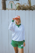 Person wearing a tropical orange tennis trucker hat with a colorful logo against a white fence background
