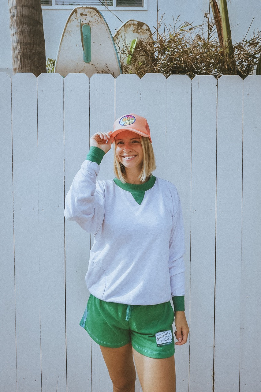 Person wearing a tropical orange tennis trucker hat with a colorful logo against a white fence background