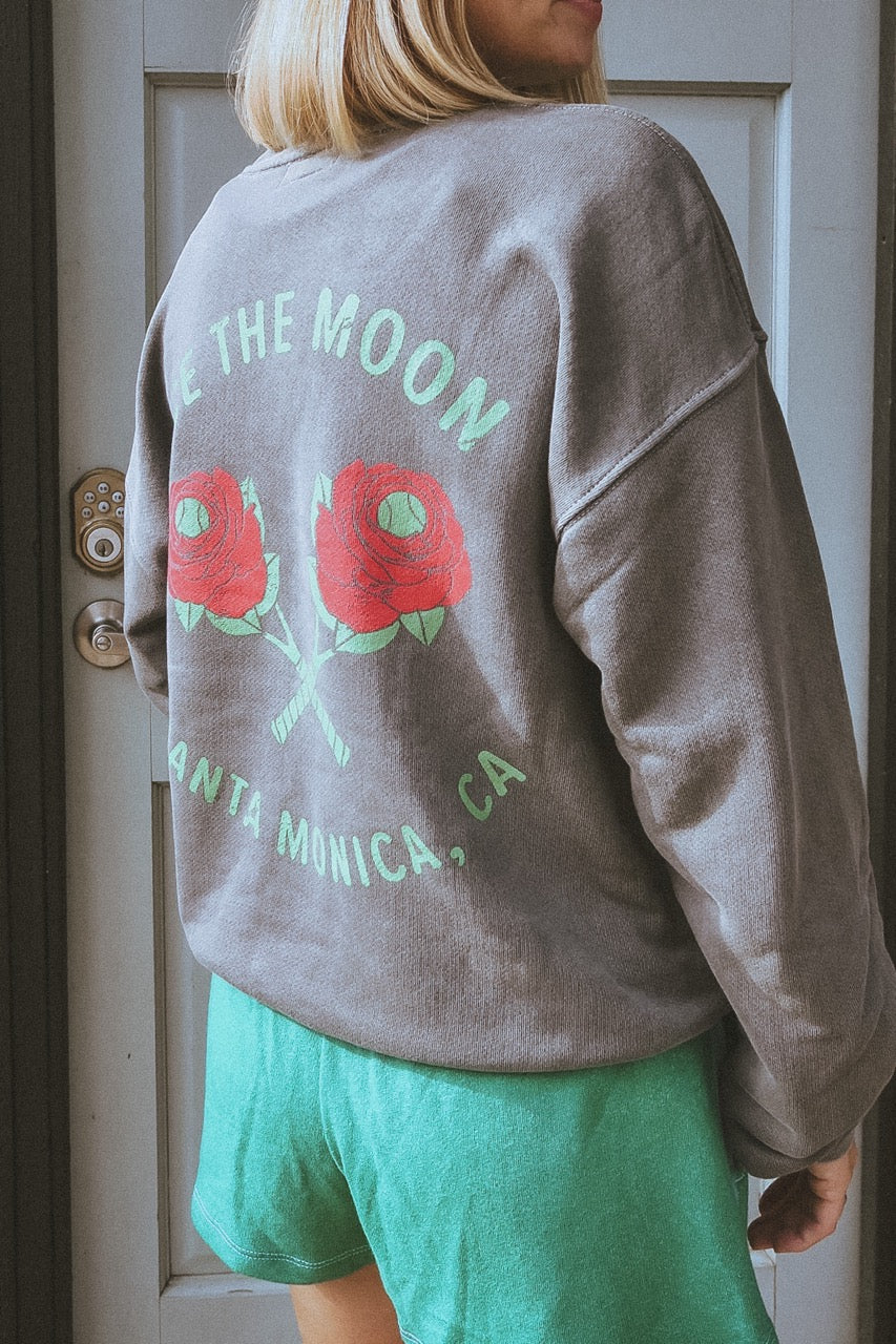 girl wearing a vintage black washed tennis crewneck sweatshirt by ace the moon tennis apparel brand that has text and rose shaped tennis rackets and santa monica, ca