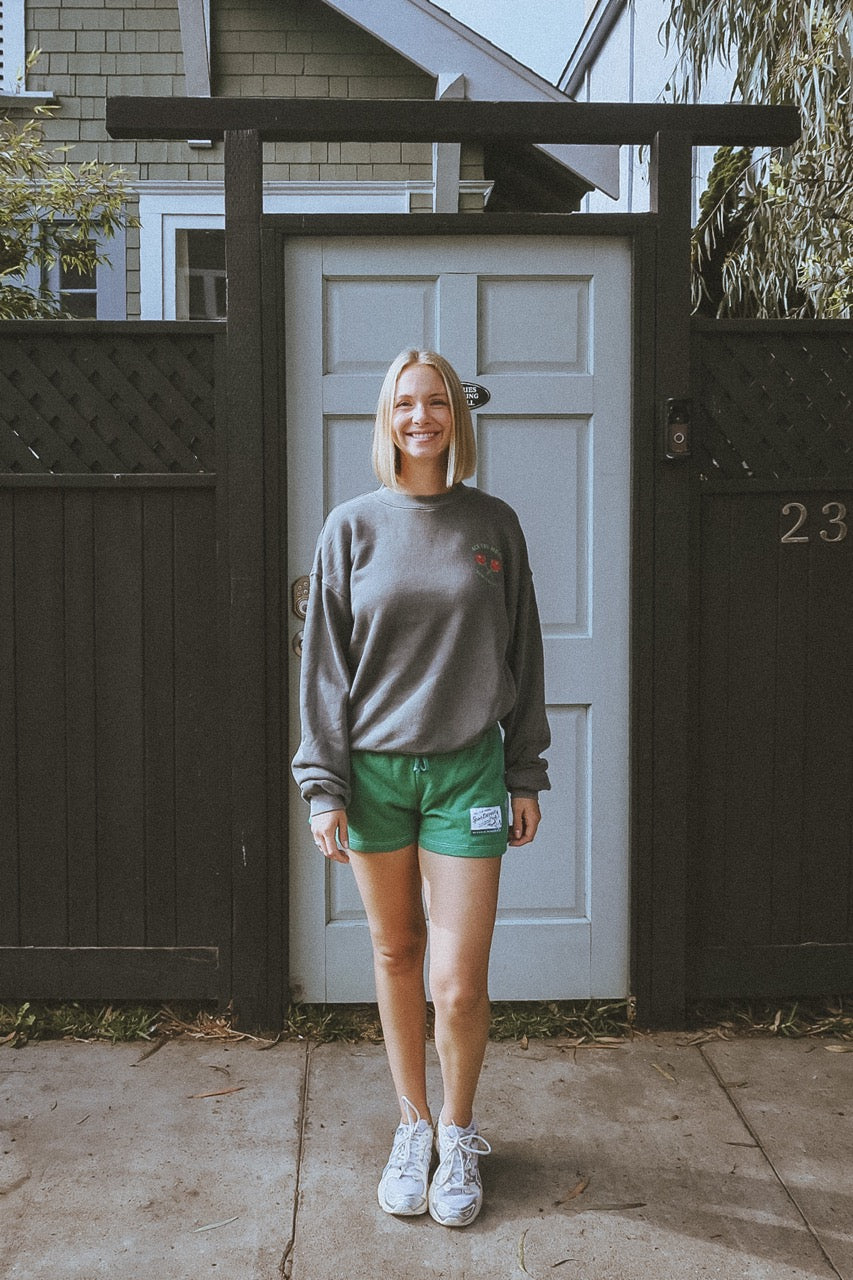girl wearing a vintage black washed tennis crewneck sweatshirt by ace the moon tennis apparel brand that has text and rose shaped tennis rackets and santa monica, ca