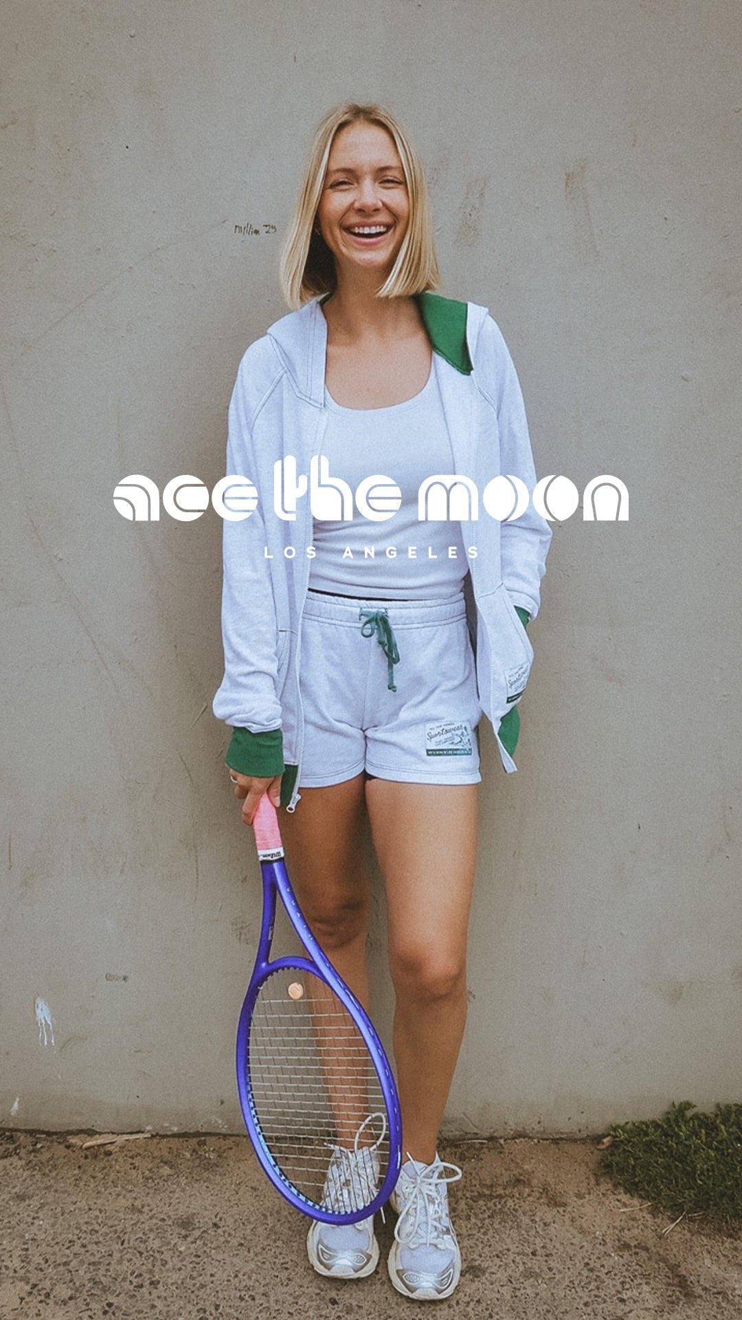 Woman holding a tennis racket with 'ace the moon' branding against a plain background