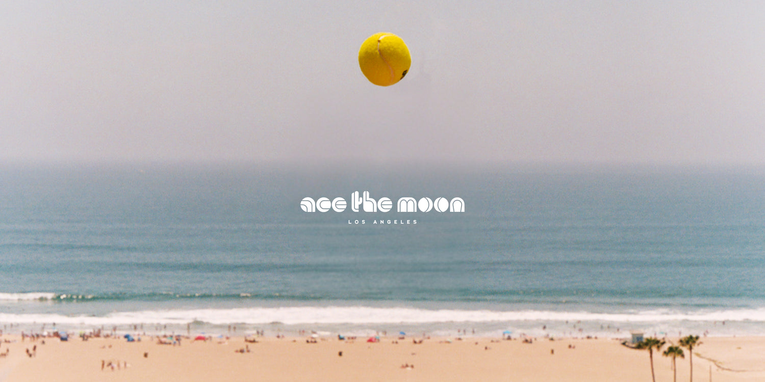 Beach scene with a large yellow tennis ball resembling the moon, text 'ace the moon' and 'Los Angeles' on a clear sky.