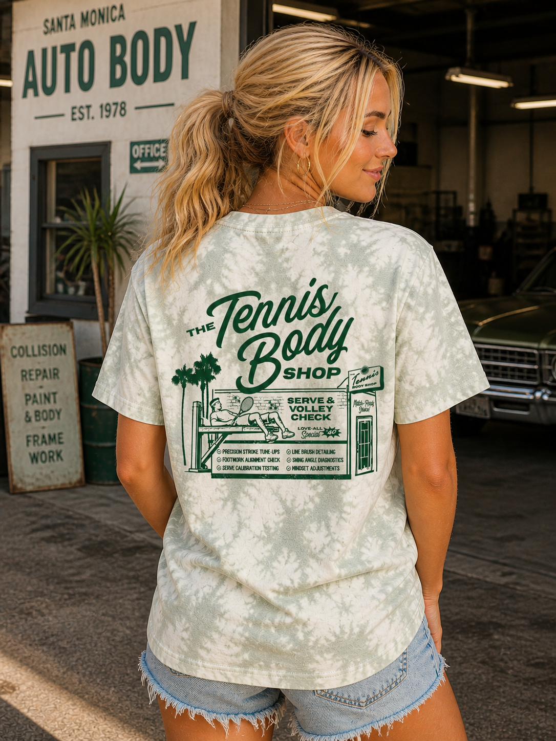 The Tennis Body Shop Tee by Ace the Moon worn by a blonde girl in a santa monica auto body shop