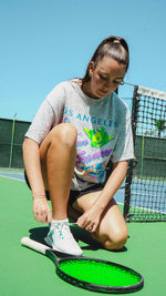 Woman on a tennis court adjusting a tennis racket with a clear blue sky in the background