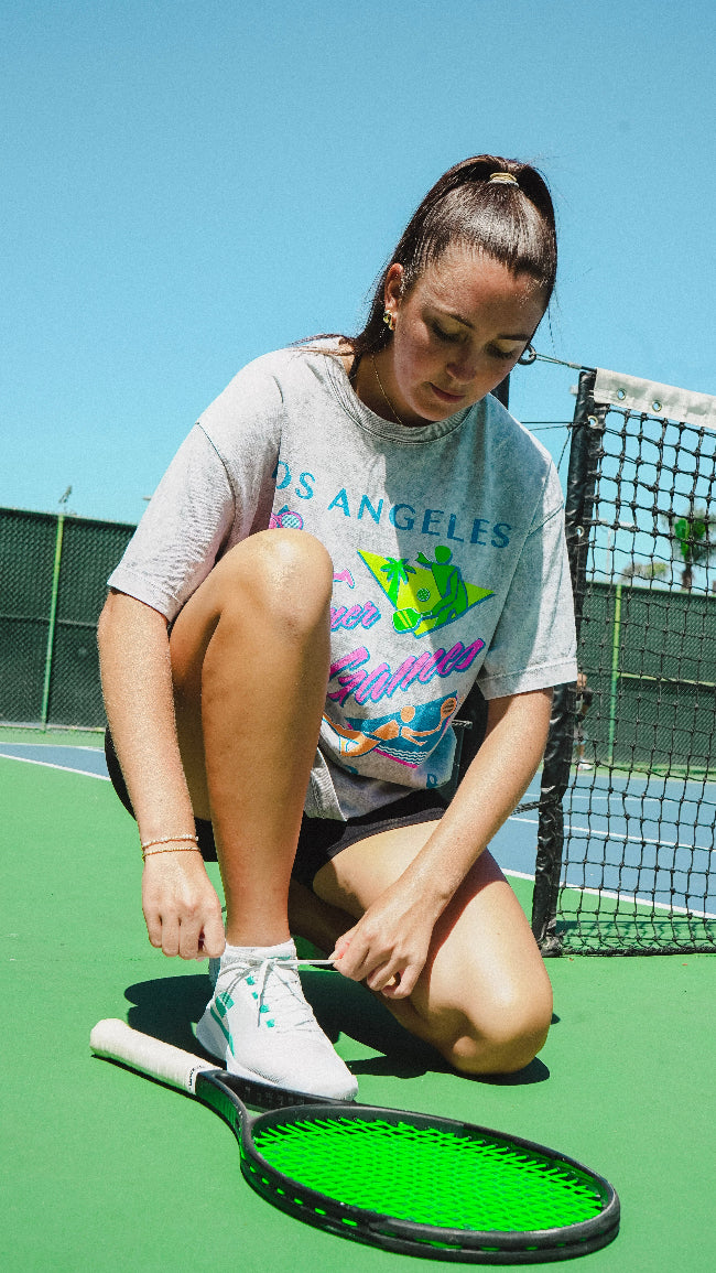Woman on a tennis court adjusting a tennis racket with a clear blue sky in the background