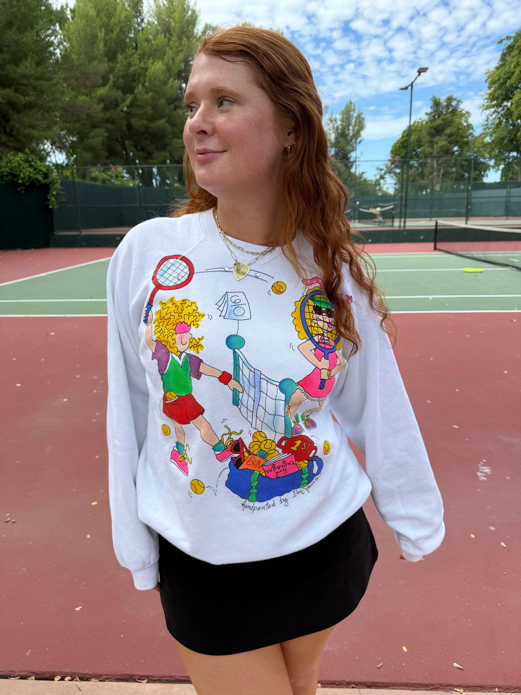 Person wearing a colorful sweatshirt with graphics on a tennis court