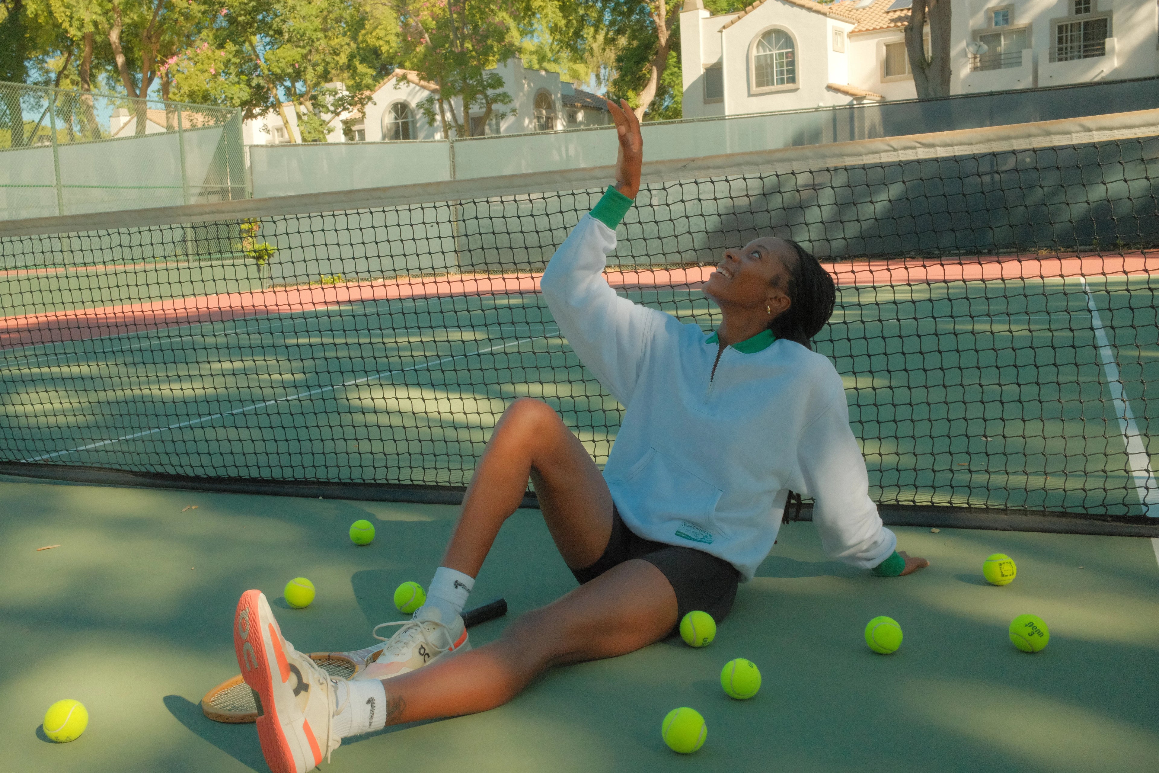 Person sitting on a tennis court with tennis balls around, holding a racket.