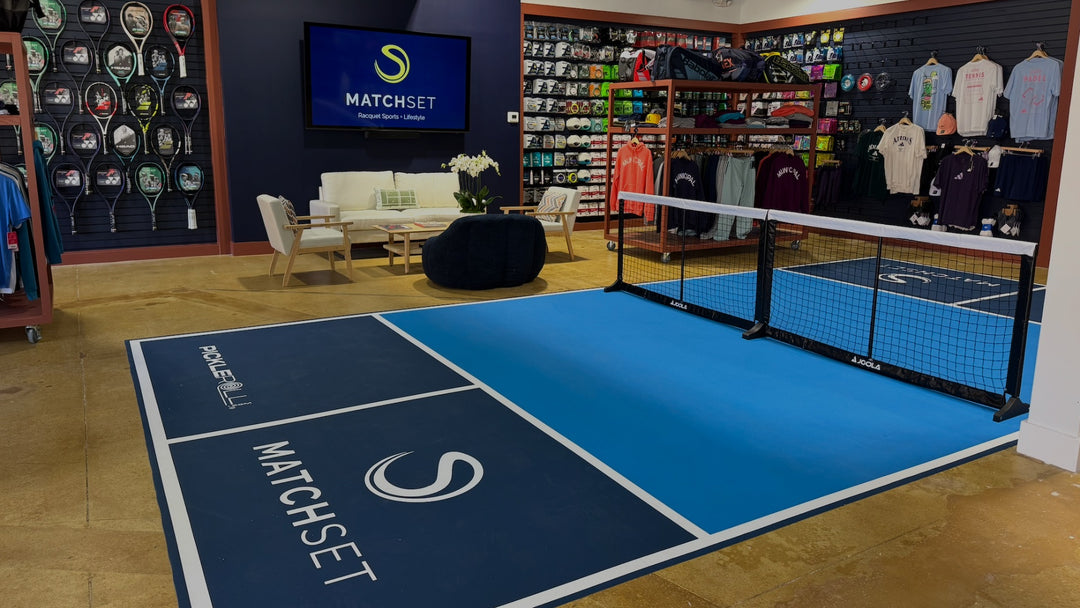 Indoor sports facility with a blue court featuring 'MATCHSET' branding, surrounded by sports equipment and furniture.
