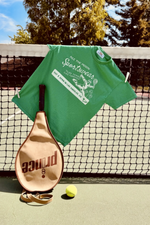 play tennis live forever tee in green by Ace the Moon tennis brand Los Angeles. picture of shirt hanging from tennis net with tennis racket and tennis ball