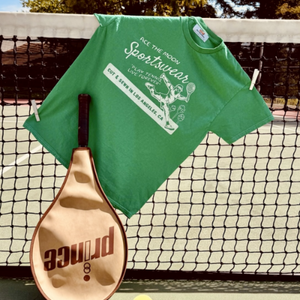 play tennis live forever tee in green by Ace the Moon tennis brand Los Angeles. picture of shirt hanging from tennis net with tennis racket and tennis ball
