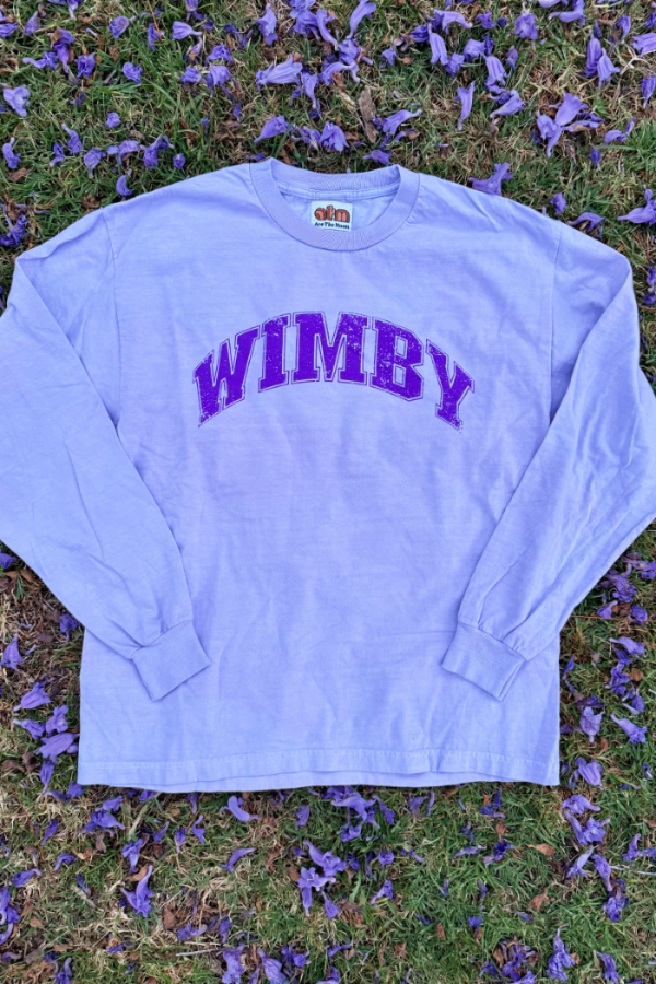 "WIMBY" long sleeve tee in vintage purple/lavender color with collegiate purple font laying on the ground surrounded by purple flower petals. made by Ace the moon premium tennis apparel brand