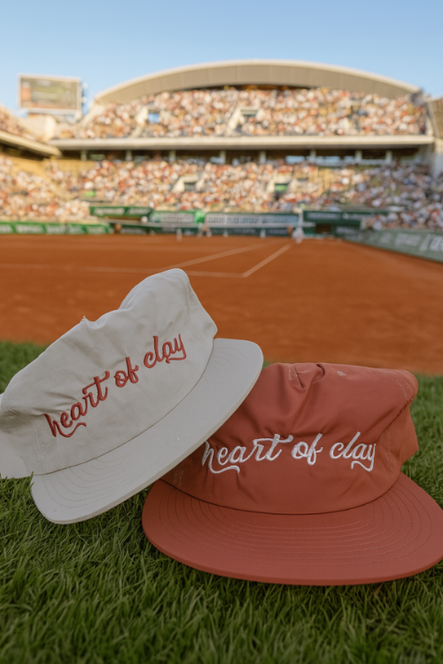 Two hats with 'heart of clay' text on a tennis court background