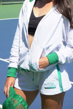Person wearing a white jacket and green shorts on a tennis court