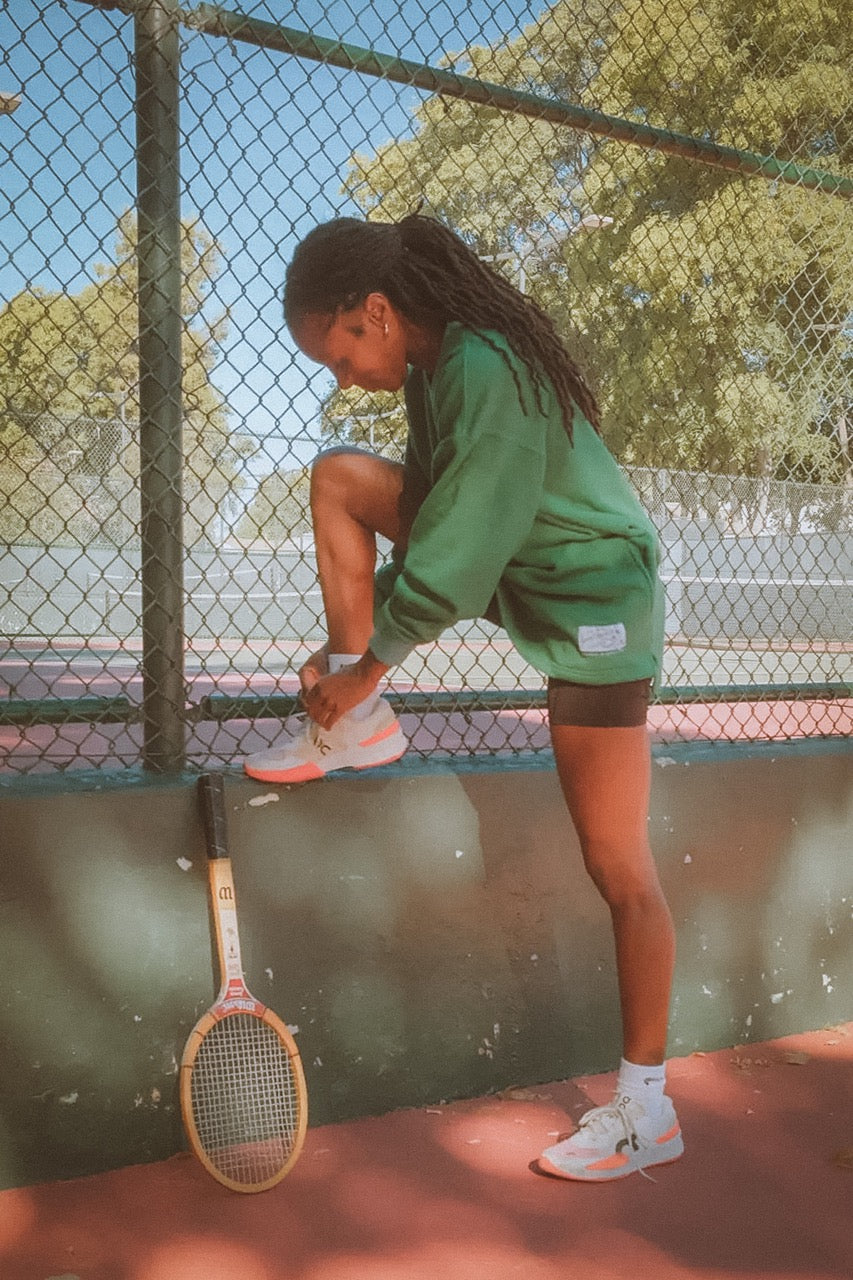 Person on a tennis court with a racket, wearing green shorts and white shoes.