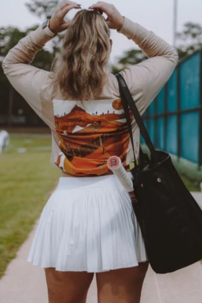 Person wearing a jacket with a colorful back design, holding a black bag outdoors.