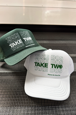 Two tennis hats, one green and one white, with text on a metallic surface.