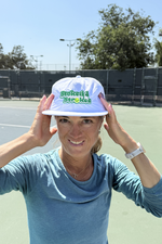Person wearing a white tennis cap with branding on a tennis court