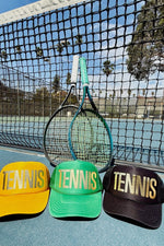 Three tennis-themed hats on a tennis court with a racket.