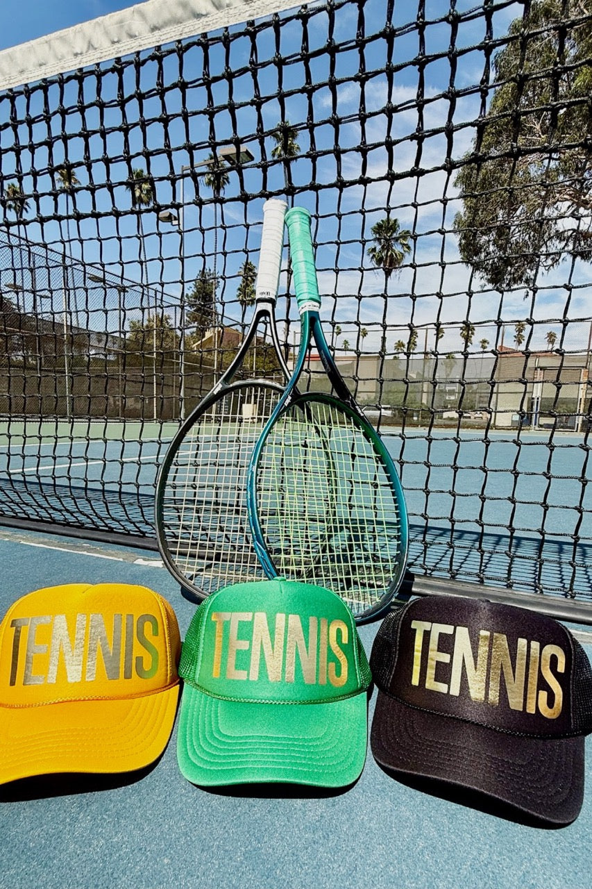 Three tennis-themed hats on a tennis court with a racket.