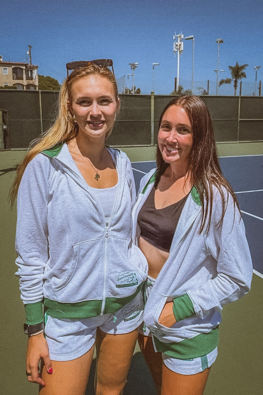 Two women standing on a tennis court wearing matching outfits.