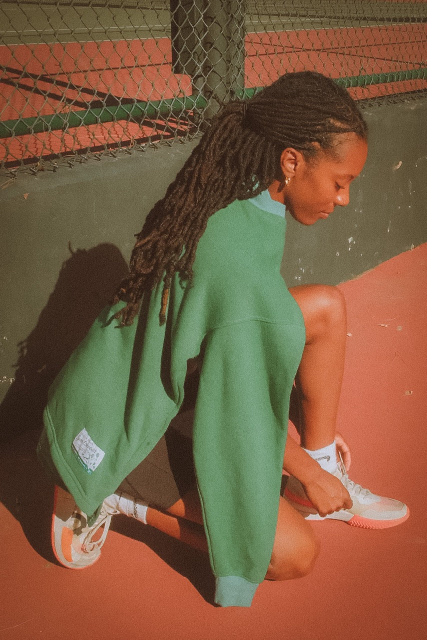 Person wearing a green sweatshirt and white sneakers on a tennis court.