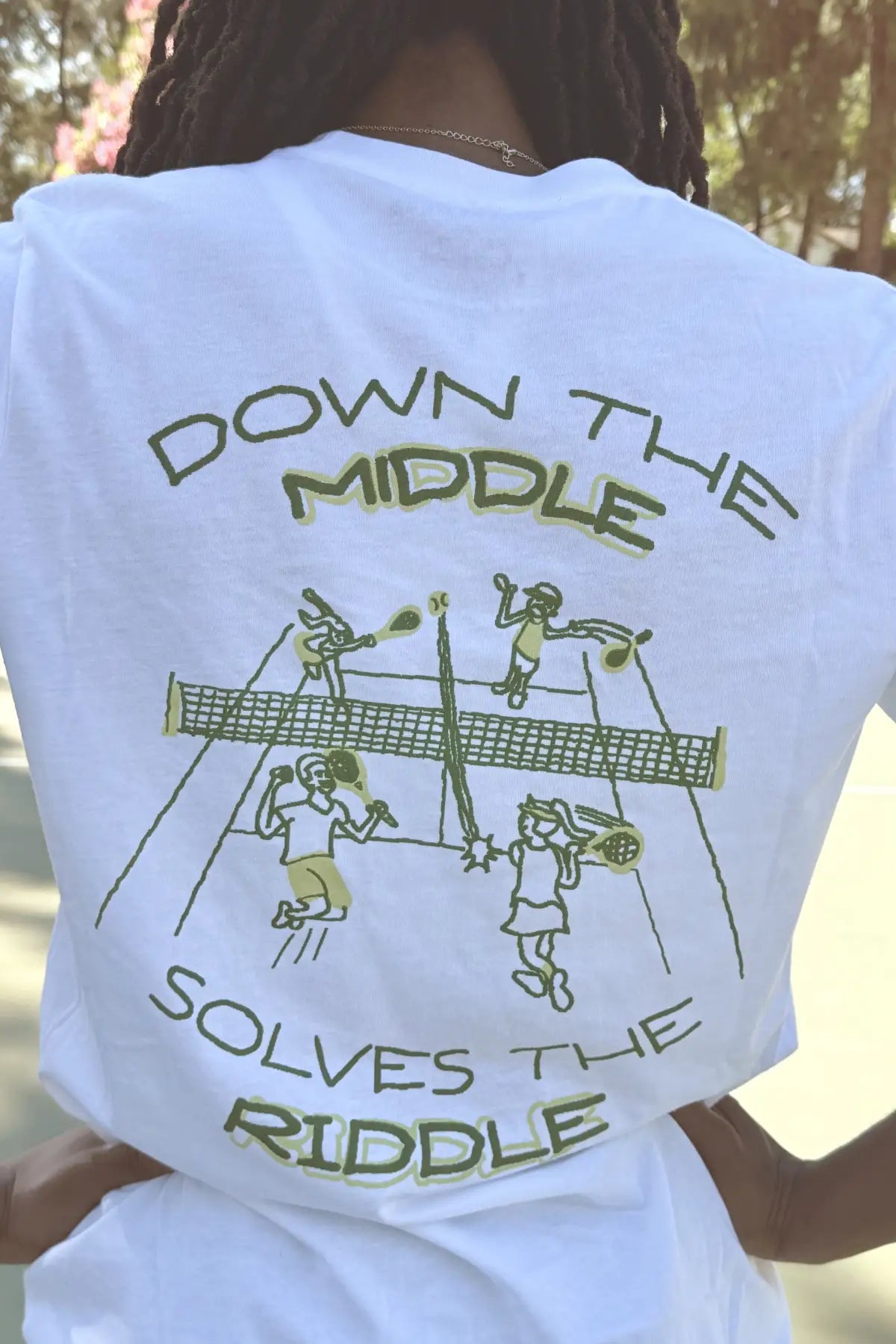 White t-shirt with green graphic and text on the back, worn by a person outdoors.
