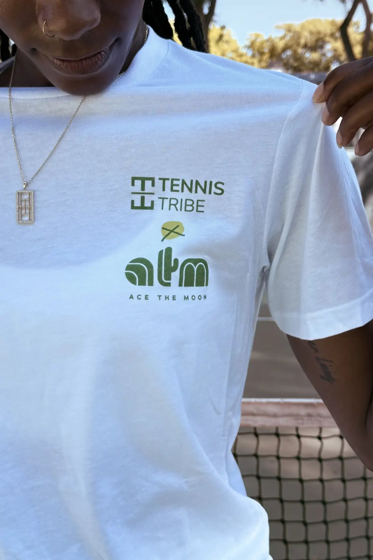 White t-shirt with 'Tennis Tribe' and 'atm' logos worn by a person.