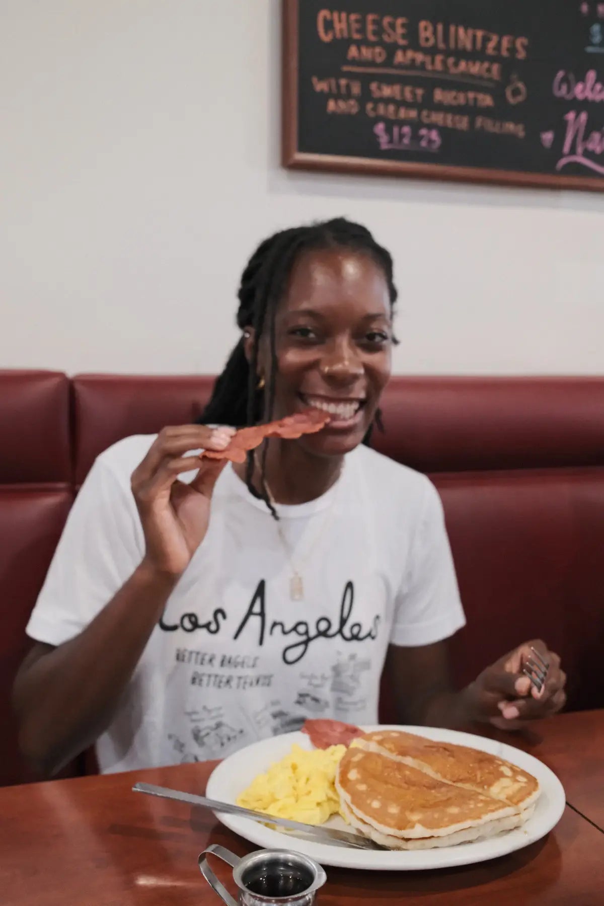 Person eating pancakes and eggs at a restaurant with a 'Los Angeles' shirt on