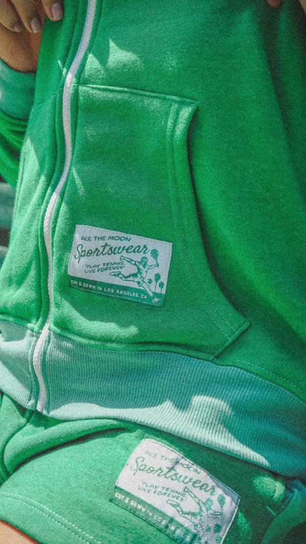 Green tennis hoodie with brand labels on a blurred background ace the moon sportswear
