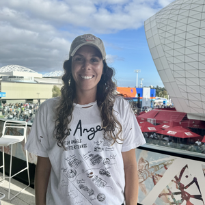 Los Angeles Tennis Bagel tour tee shirt in white by Ace the Moon Premium athleisure apparel brand. shirt worn by a woman standing in front of a tennis stadium
