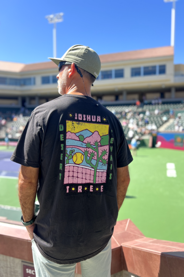 joshua tree desert tennis tee in black by Ace the Moon premium athleisure apparel brand worn by a man standing at a tennis stadium