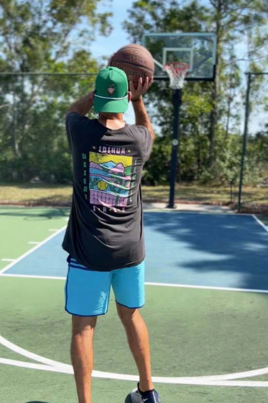 Person taking a basketball shot on an outdoor court with trees in the background