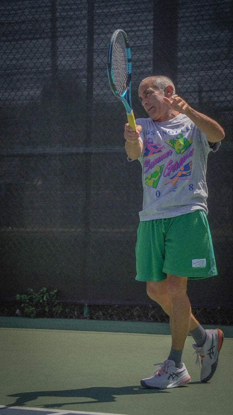 Person playing tennis on a court with a racket wearing ace the moon's los angeles summer games tee