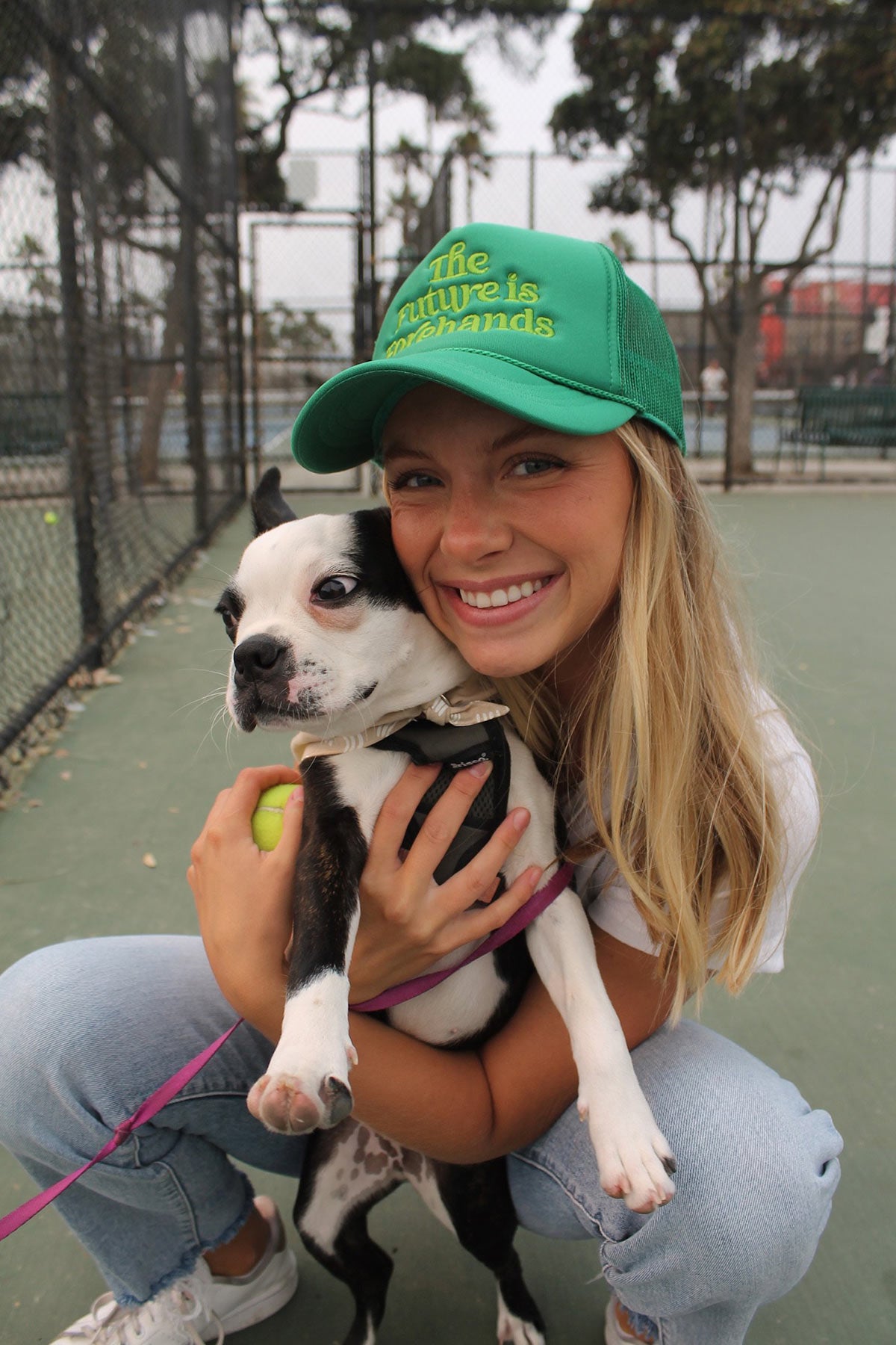 the future is forehands tennis trucker hat in green by Ace the Moon tennis apparel brand LA worn by a girl holding a cute puppy on a tennis court