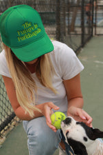 the future is forehands tennis trucker hat in green by Ace the Moon tennis apparel brand LA worn by a blonde girl playing with a puppy and a tennis ball on a tennis court