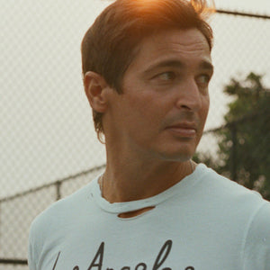 Los Angeles Tennis Bagel tour tee shirt in white by Ace the Moon Premium athleisure apparel brand. shirt worn by a male model looking away